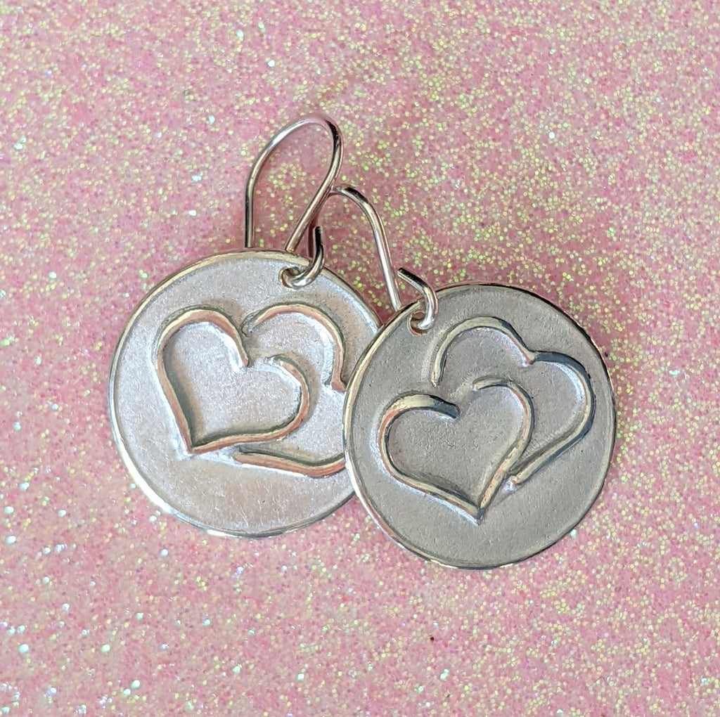 DISC OF HEARTS EARRINGS | < Z-FIRE.COM > Two hearts are highlighted and polished on a silver disc with a frosted background and highlighted and polished edges.  .950 Fine Silver Disc About 11/16" Diameter  About 1.8 cm Diameter .925 Sterling Silver Ear Wires