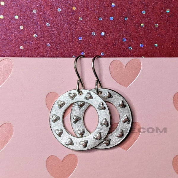 RING OF HEARTS EARRINGS | < Z-FIRE.COM > Tiny hearts are highlighted and polished on flat silver rings with a frosted background and highlighted and polished edges.  .950 Fine Silver Rings About 11/16" Diameter  About 18 mm Diameter .925 Sterling Silver Ear Wires